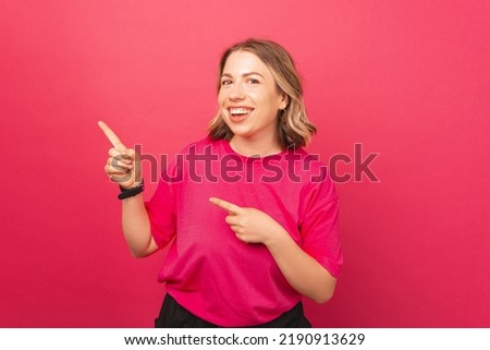 An exciting happy woman is pointing at free space near a pink background