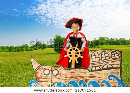 Boy as pirate stands on ship and holds the helm