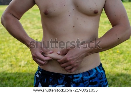 Man without shirt holding his fat belly on nature background