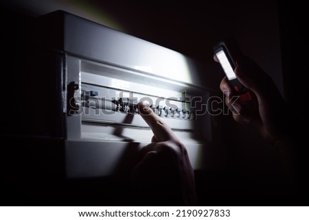 Blackout concept, energy crisis. Hand holding a flashlight to investigate a home fuse box Royalty-Free Stock Photo #2190927833