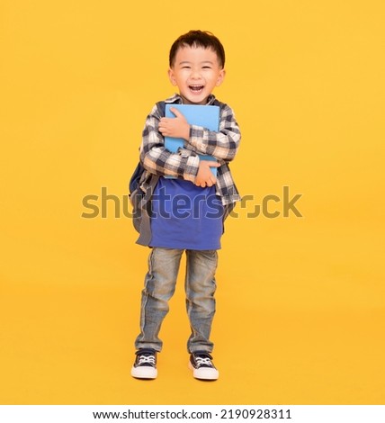 happy asian kid holding or hugging  big book over yellow background Royalty-Free Stock Photo #2190928311