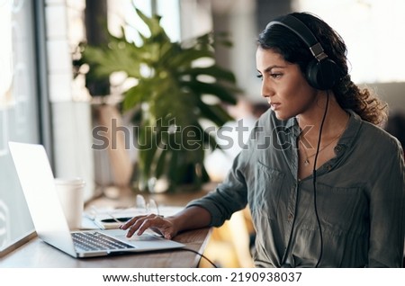 Female student working on laptop with headphones for a university project in a cafe, restaurant or coffee shop. Thinking and studying young university or college woman typing and listening to music Royalty-Free Stock Photo #2190938037