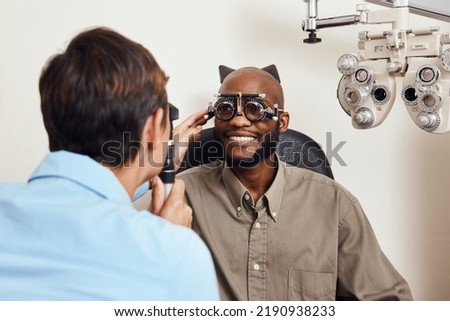 Optical exam, optician or eye doctor at work testing vision or sight of patient at optometrist. Happy, smiling young man checking his eyes for glasses or treatment at an ophthalmologist in a clinic. Royalty-Free Stock Photo #2190938233