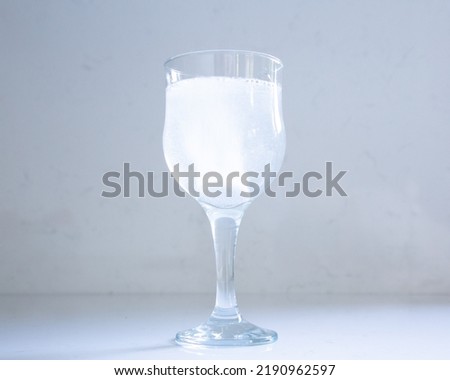 Selective focus closeup of stem glass set on quartz background, with effervescent antacid tablet dissolving in water