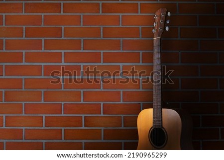 acoustic guitar stand in front of brick wall background. body part front made with top solid, side and back mahogany wood.