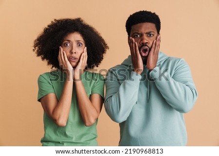 Black man and woman expressing fear and looking at camera isolated over beige background
