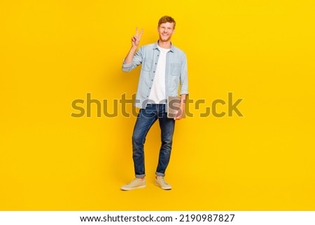 Full length photo of young happy programmer guy hold laptop showing v-sign friendly isolated on yellow color background