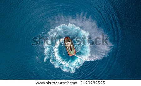 Aerial drone photo of tow - tug boat assisting by pulling or pushing huge container ship to anchor in terminal port Royalty-Free Stock Photo #2190989595