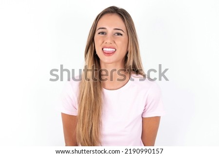young beautiful woman wearing pink T-shirt over white background with happy and funny face smiling and showing tongue.