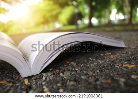 Book open on asphalt local road straight forward to the forest green environment area. Travel and education concept.