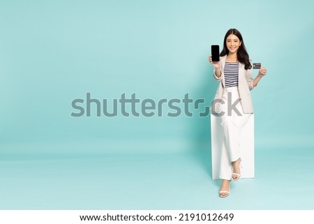 Young Asian businesswoman sitting and showing credit card and mobile phone isolated on green background Royalty-Free Stock Photo #2191012649
