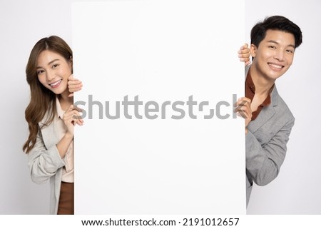 Asian businessman and businesswoman is standing behind the white blank banner or empty copy space advertisement board isolated on white background