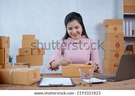 Young owner business woman received orders clients and writing on the products in parcel cardboard box packaging.