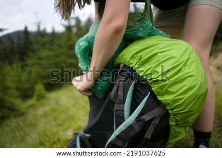 A girl puts a rain cover on her tourist backpack during a hike in the mountains in summer, close-up hands. Royalty-Free Stock Photo #2191037625