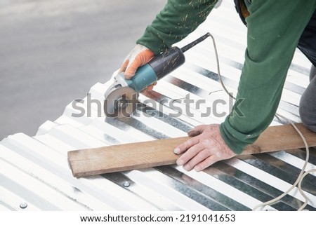 The worker cuts a metal sheet for installation on the roof of the house. 