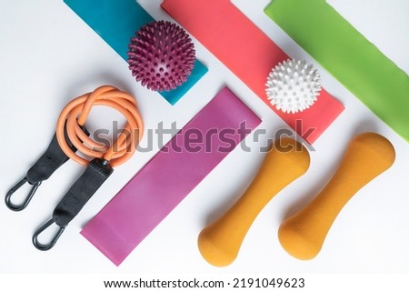 Different colourful equipment for fitness and sport exercises orange dumbbells and expanders, fitness balls and bands lying on a white background
