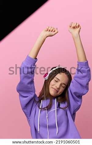 vertical photo of a happy, attractive woman laughing, dancing with pleasure, listening to music with headphones, eyes closed, standing on a pink studio background
