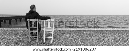 Lonely man sitting on chair and watching distant sea. Loneliness  concept, black  white photography. Large copy space for ad or advertising text. High resolution photo for big display, print, banner.