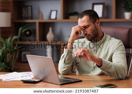 Tired african american businessman after exhausting paperwork taking off eyeglasses and feeling eye strain. Head ache, bad vision, chronic fatigue and eyestrain concept. Burnout and overwork concept Royalty-Free Stock Photo #2191087487