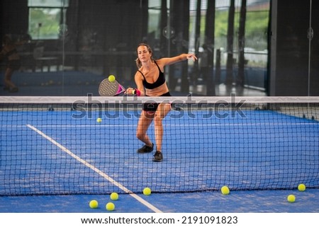 Woman playing padel in a blue grass padel court indoor - Young sporty woman padel player hitting ball with a racket Royalty-Free Stock Photo #2191091823