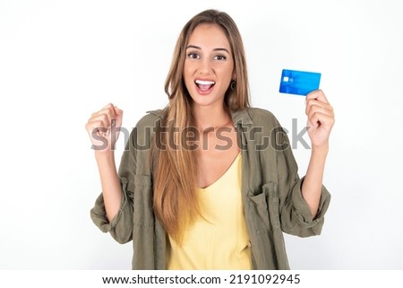 Photo of lucky impressed young beautiful woman wearing green overshirt over white background arm fist holding credit card. Celebrated
