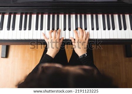 Top view of woman's hands playing piano by reading sheet music.  Royalty-Free Stock Photo #2191123225
