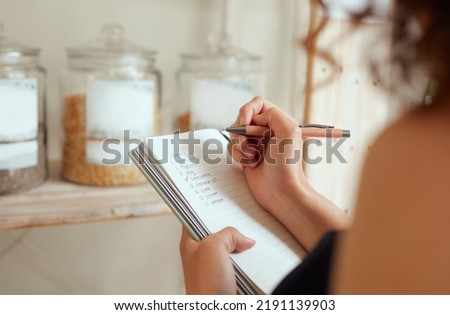 Budget planning, making shopping list and managing household expenses to save money. Financial accountability at home. Woman making shopping list for groceries on a notebook to plan a meal for Royalty-Free Stock Photo #2191139903