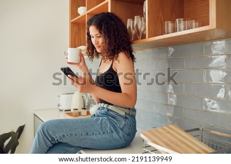 Woman texting, chatting on the phone while relaxed, carefree and sitting on kitchen counter. Young, relaxing and casual female student at home looking at social media, pictures or videos