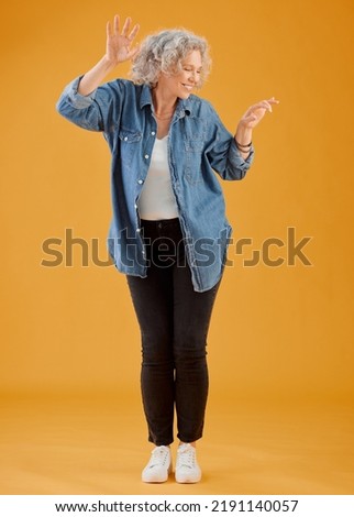 Fun, happy and cheerful woman dancing, celebrating and enjoying life alone against an orange background. Senior woman feeling excited, joyful and playful with dressed stylish, trendy and fashionable Royalty-Free Stock Photo #2191140057