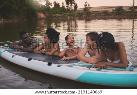 Friends, vacation and having fun while leaning on a paddle board and talking in a lake. Happy and diverse people laughing while enjoying the water and friendship on their holiday and nature travel