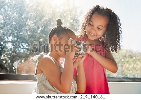 Cute sisters bonding, taking photos on camera at home, smiling while being playful and curious. Little girls playing, having fun together, enjoying their bond and sharing precious childhood moments