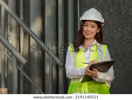young engineer woman wearing white hard hat and suresafe safty vest holding clipboard checking standing inindustrial site Royalty-Free Stock Photo #2191140551
