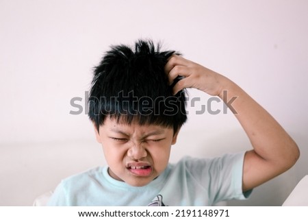 A Little Asian boy itchy his hair.