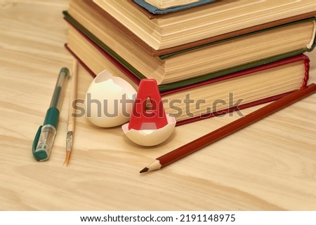 a stack of books writing materials and a split chicken egg with the letter a inside on the table concept knowledge education school. High quality photo