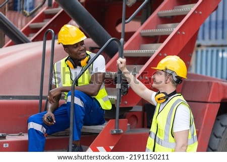 Young Caucasian man and African American worker work in container site. Attractive handsome male laborer standing and talking together after process orders at warehouse logistic in cargo freight ship.