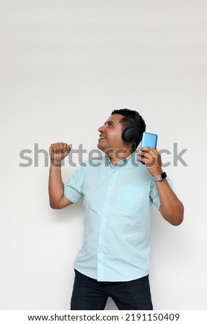 Latin adult man uses his wireless headphones and cell phone to listen to music, dance, relax and enjoy technology
