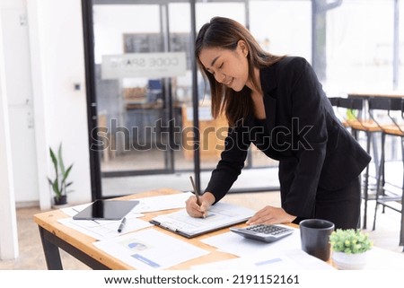 Charming businesswoman standing at the office taking notes on documents.