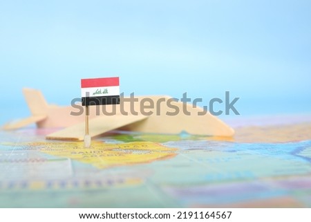 Selective focus of Iraqi flag in blurry world map and wooden airplane model. Iraq as travel and tourism destination concept.