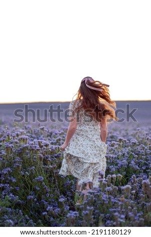 A girl runs across a field of purple phacelia flowers, her hair fluttering in the wind.