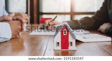 Miniature of cottage house on table close up view, happy African family, agency or bank clients handshake real estate agent after contract signing, on blurred background.
