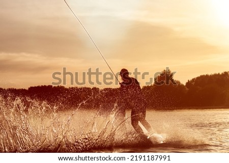 Wakeboarder making tricks. Low angle shot of man wakeboarding on a lake. Man water skiing at sunset.