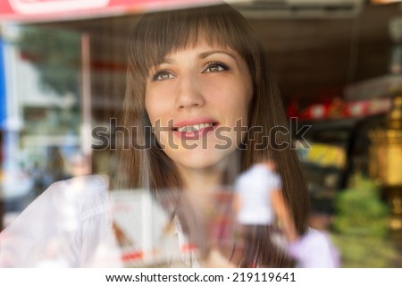 Beautiful smiling girl drinking coffee and looking out through window in cafe. Dreaming fancying young woman at the restaurant