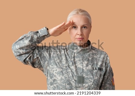 Mature female soldier saluting on beige background