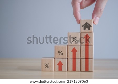 Real estate concept. House, property investment, asset management, Interest rates, loan mortgage, house tax. Hand holding house icon on wooden block from stack of block with percent and rise of arrow. Royalty-Free Stock Photo #2191209063