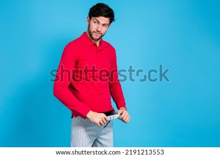 Youth Funny Concepts. Caucasian Handsome Brunet Man in Striped Underware Pulling Pants While Looking Aside Against Seamless Blue Background. Horizontal Image
