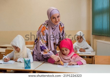 Female hijab Muslim teacher helps school children to finish the lesson in the classroom.	