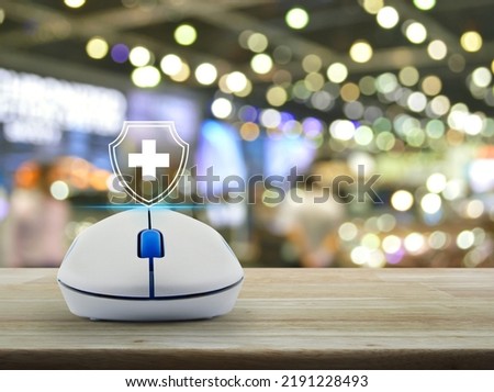 Cross shape with shield flat icon on wireless computer mouse on wooden table over blur light and shadow of shopping mall, Business healthy and medical care insurance online concept