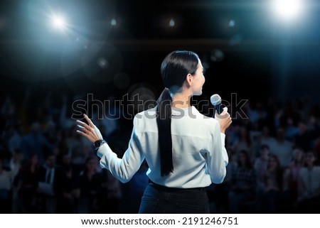 Motivational speaker with microphone performing on stage, back view