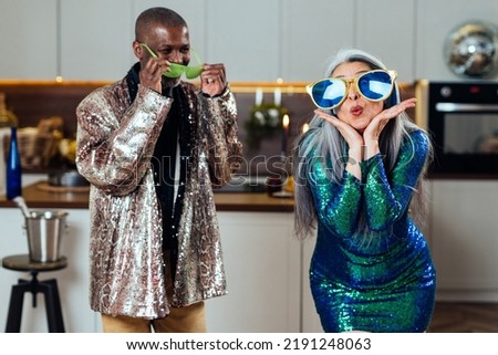 Cinematic image of an happy multiethnic senior couple making party. Indoors Lifestyle moments at home. Concept about seniority and relationships