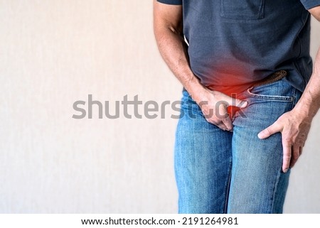 A man holds his crotch with his hand. The place of pain is marked in red. Urinary incontinence, enuresis. Inflammation of the bladder. The concept of medicine. Royalty-Free Stock Photo #2191264981